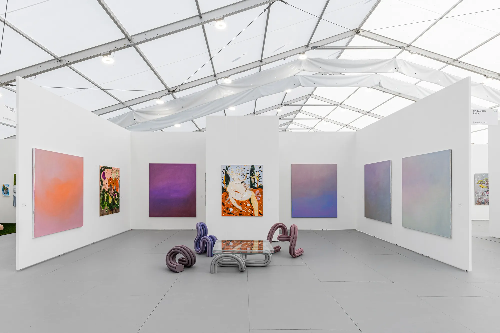 Installation view of Carvalho Park’s booth at Untitled Art, Miami Beach 2022 featuring paintings by Yulia Iosilzon and Maximilian Rödel and chairs by Ara Thorose. Courtesy of Carvalho Park.
